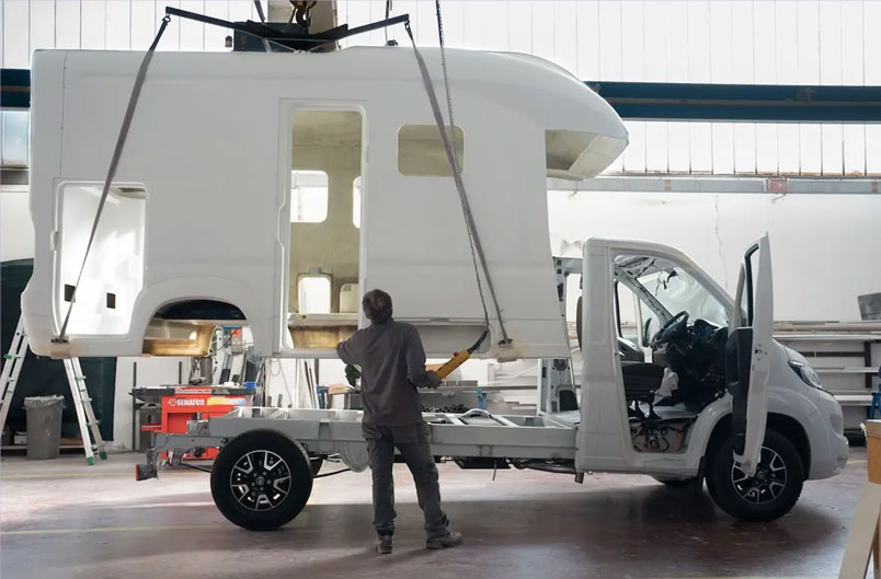 A worker lowers the monocoque shell onto the motorhome chassis